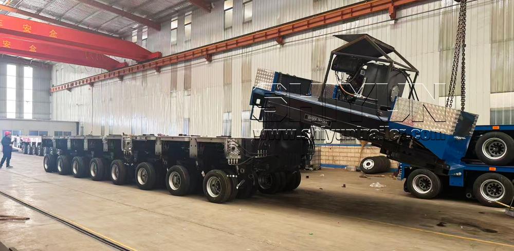 Crane loading heavy machinery onto modular trailer