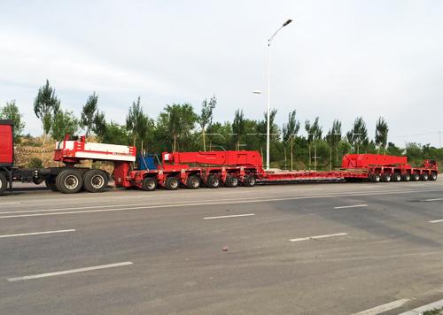 Red girder trailer transporting long cargo on road